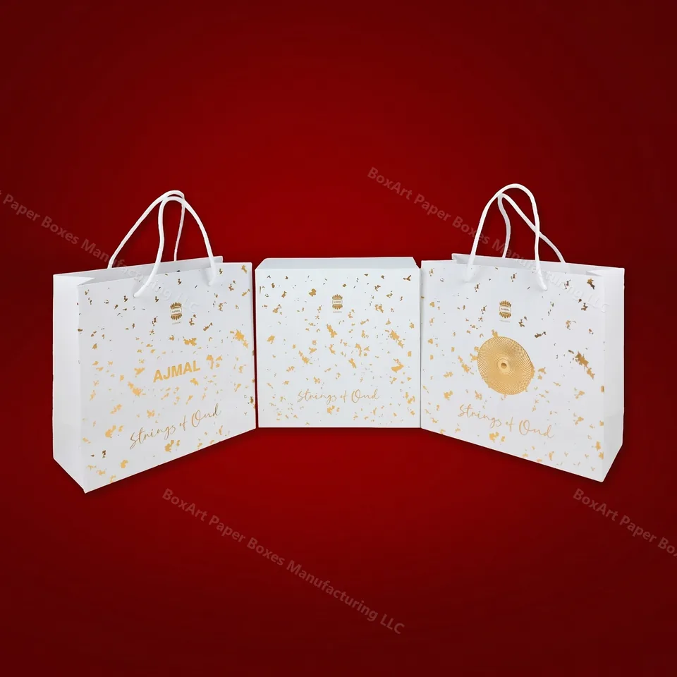 Ajmal Strings of Oud — Retail Set — luxury shopping bags manufactured in Dubai by BOXART — Matching retail set — twin gold-fleck shopping bags flanking the Strings of Oud gift box for boutique presentation.
