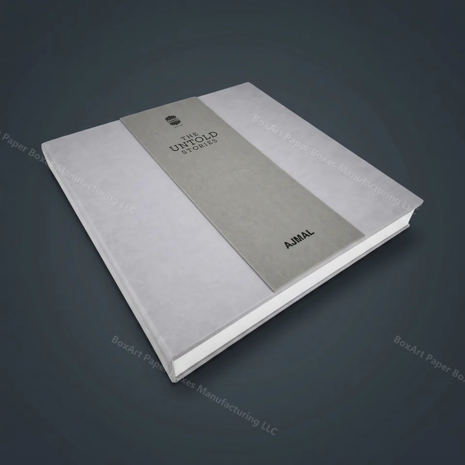 Ajmal — The Untold Stories Book Box — luxury corporate gifting manufactured in Dubai by BOXART — Grey suede-wrapped rigid book with contrast band and blind-deboss branding — Ajmal heritage edition.