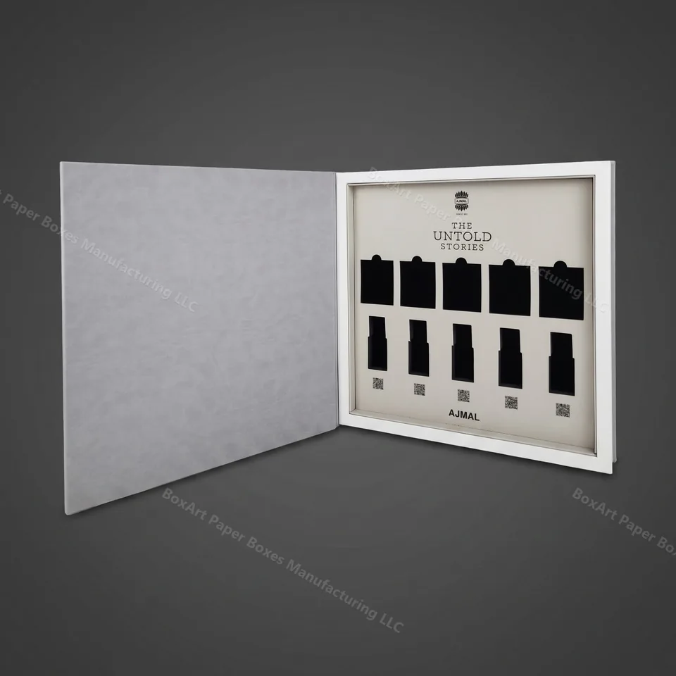 Ajmal Untold Stories — 10-Bottle Book Box — luxury perfume boxes manufactured in Dubai by BOXART — Book-style rigid box with grey suede wrap, custom-die inserts for ten perfume bottles and QR-coded storytelling panels.