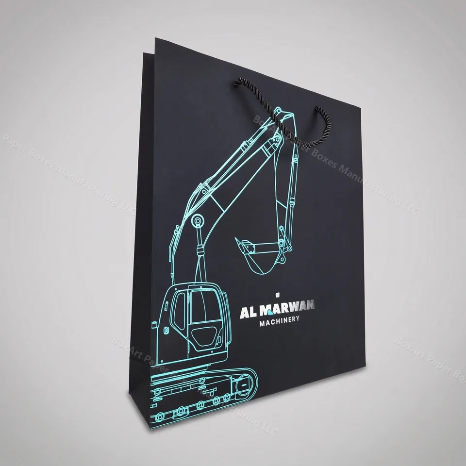 Al Marwan Machinery Shopping Bag — luxury shopping bags manufactured in Dubai by BOXART — Premium matte black paper bag with rope handles, cyan foil-stamped excavator line-art on both faces.